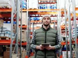 A man holding a tablet computer standing in a warehouse full of shelves