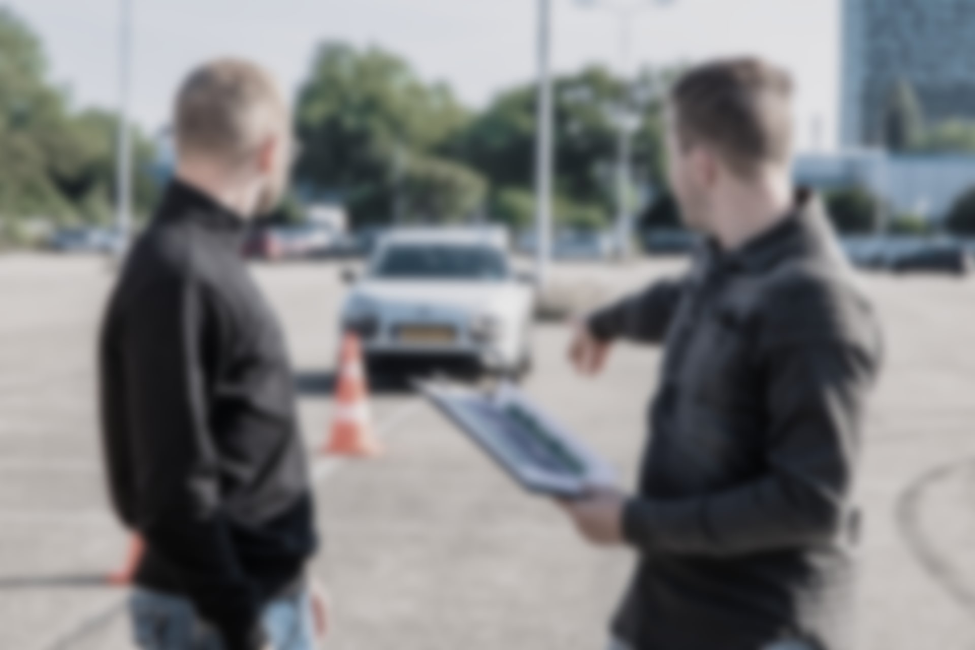 A driving instructor holding a clipboard points at a car parked behind a traffic cone